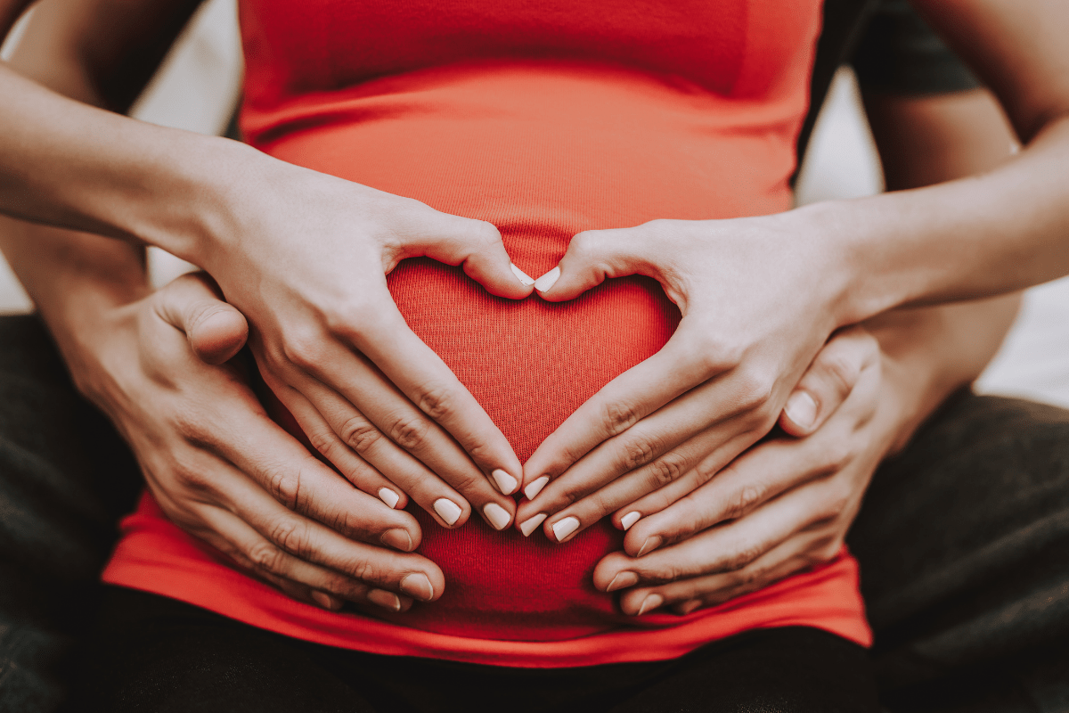 A pregnant woman gently holding her stomach with care, while a man supports her from behind