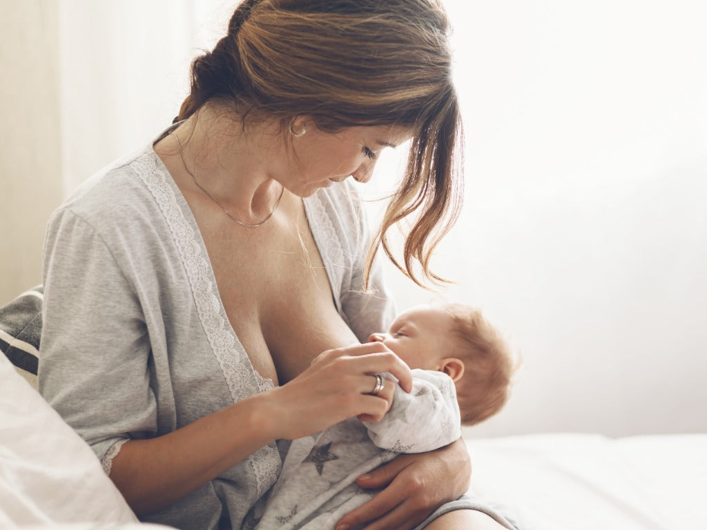 A mother sitting in bed, cradling her baby and breastfeeding with love and care
