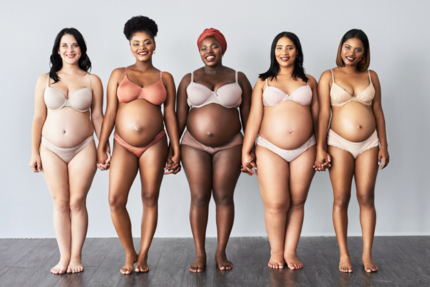 Five pregnant mothers from different races standing in underwear and holding hands