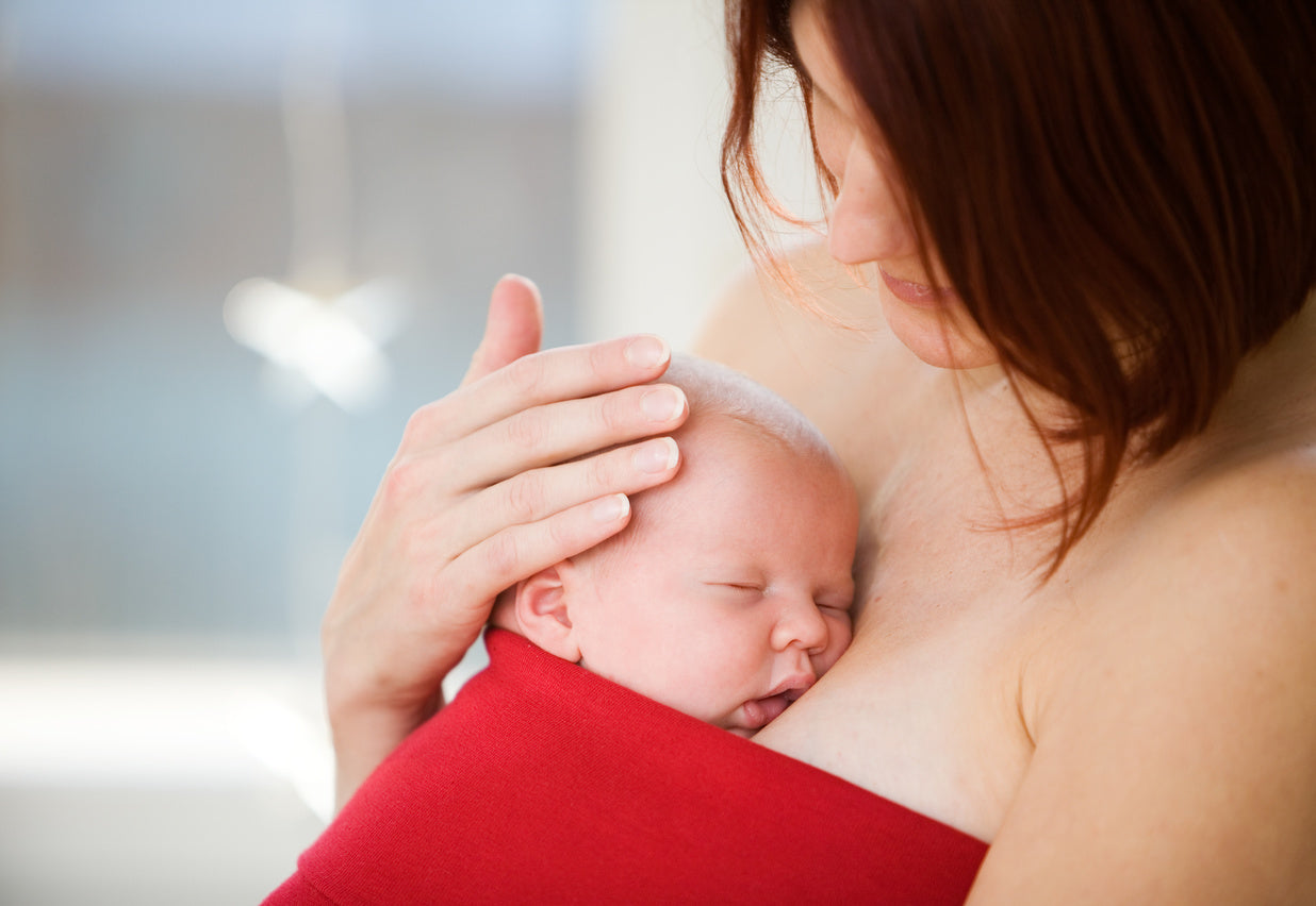 Mother holding a newborn baby in skin to skin contact against her breast