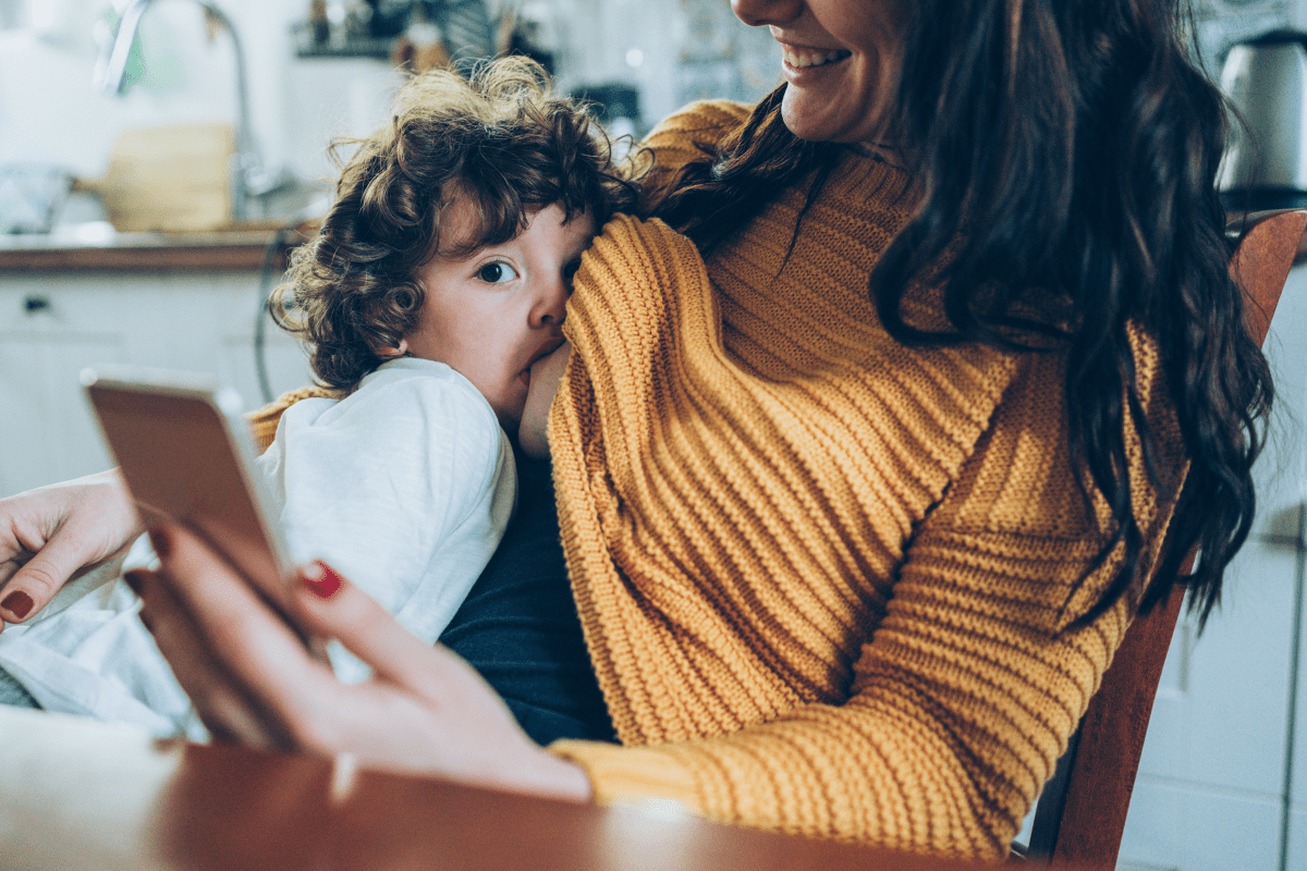 Mother is breastfeeding while reading ‘Protecting your mental wellbeing while breastfeeding’ -e-guide on her phone