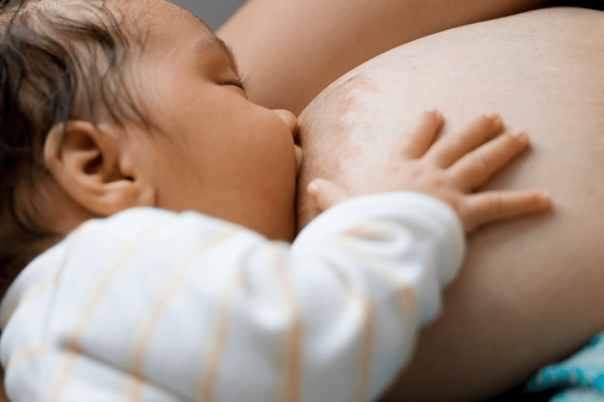 A baby peacefully nursing and drinking breast milk directly from its mother's breast