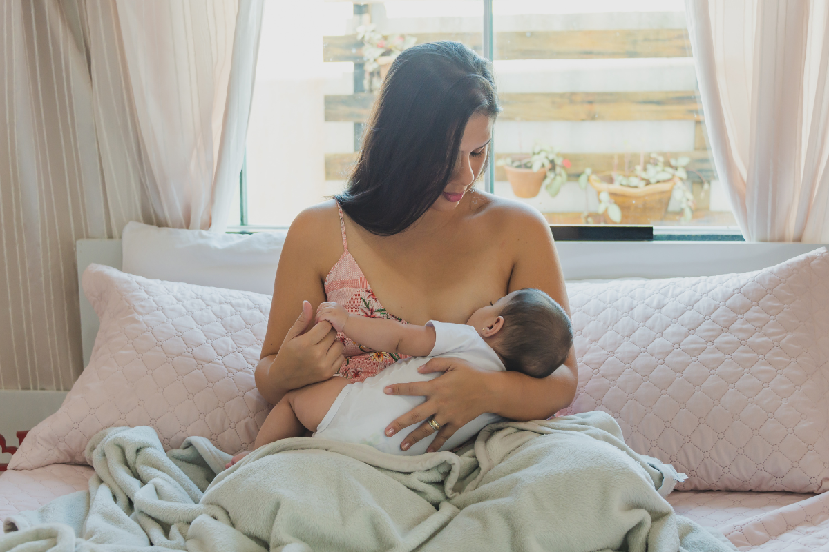 A mother nurturing her baby through breastfeeding on top of the bed
