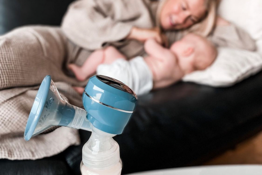 Lola&Lykke Smart Electric Breast Pump showcased alongside a mother lying on a couch with her baby in the background