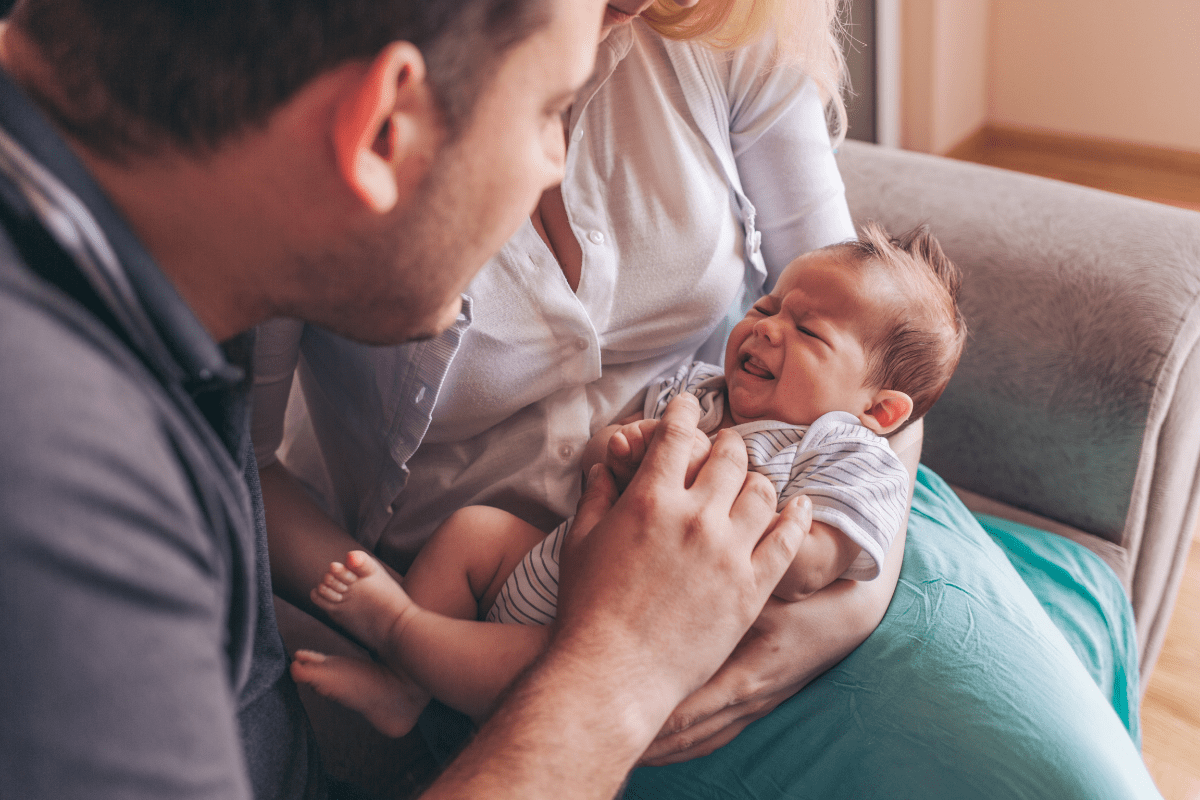 A distressed baby with colic crying in the comforting arms of their parents.