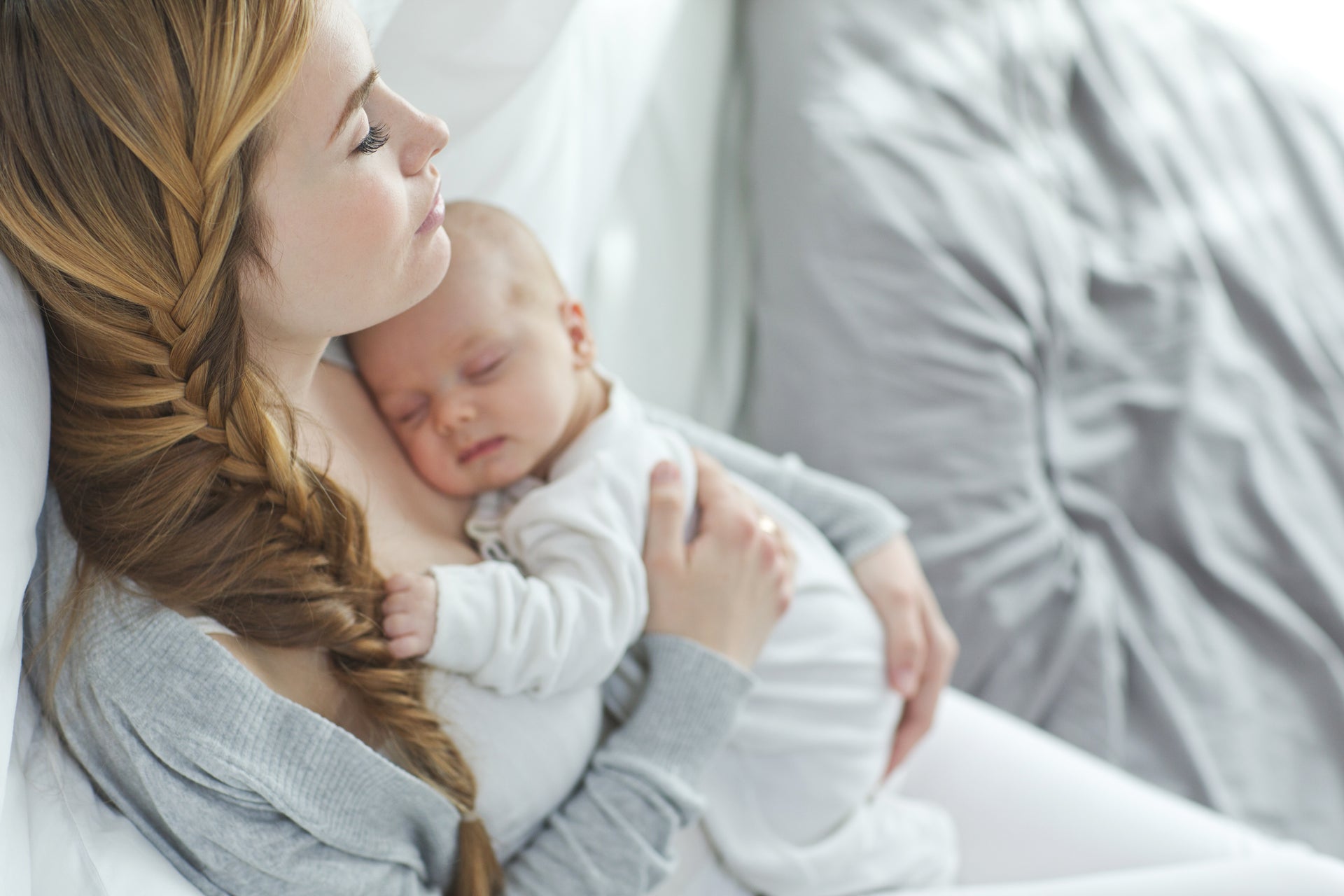 Tired mother cradling a baby in her arms while lying in bed