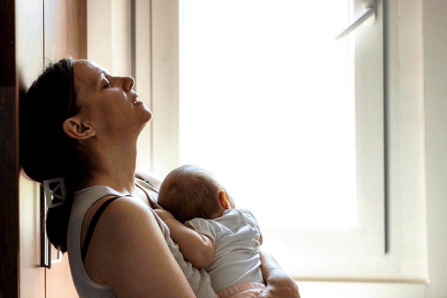  A tired woman with postpartum anemia holds a baby in her arms while sitting on the floor