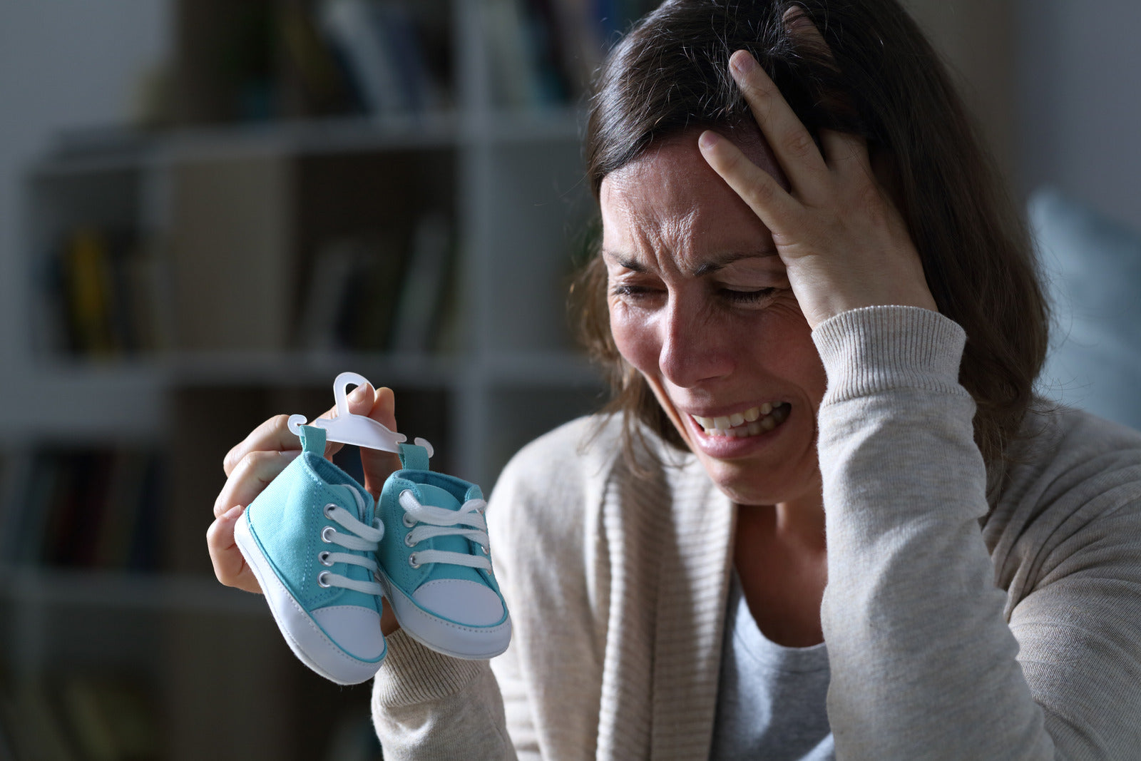 Woman crying and feeling sadness over her miscarriage while holding up a pair of blue baby booties