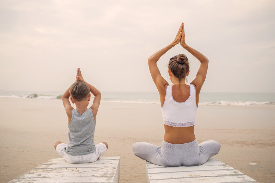 Fulfilled mom with her child on a beach doing yoga