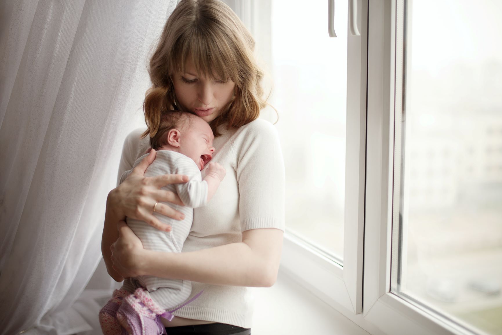 A mother holding her crying baby in front of the window
