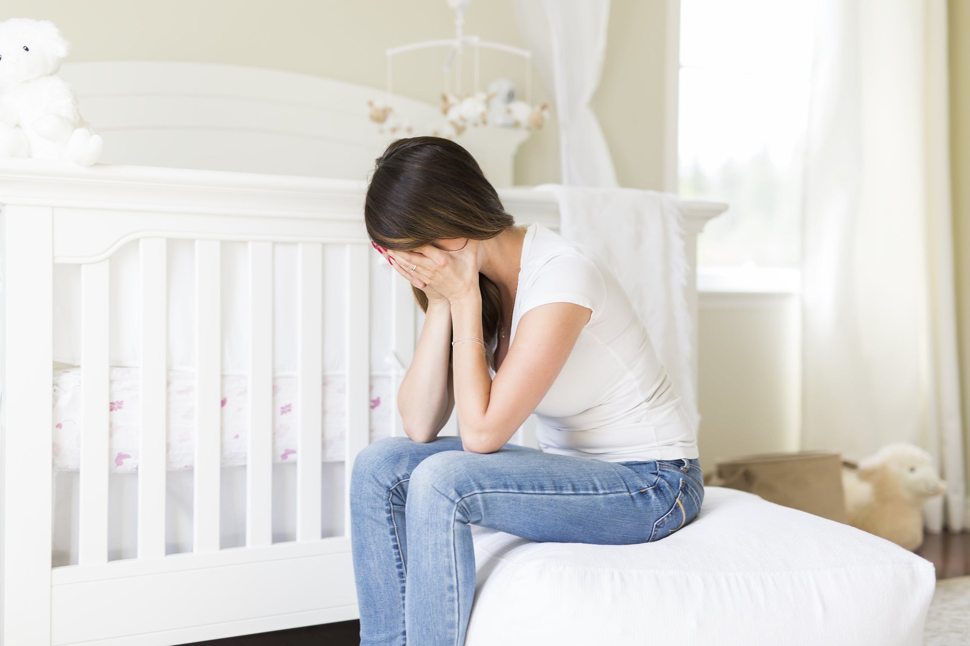 Tired and exhausted new mum sitting down while covering her face with her hands