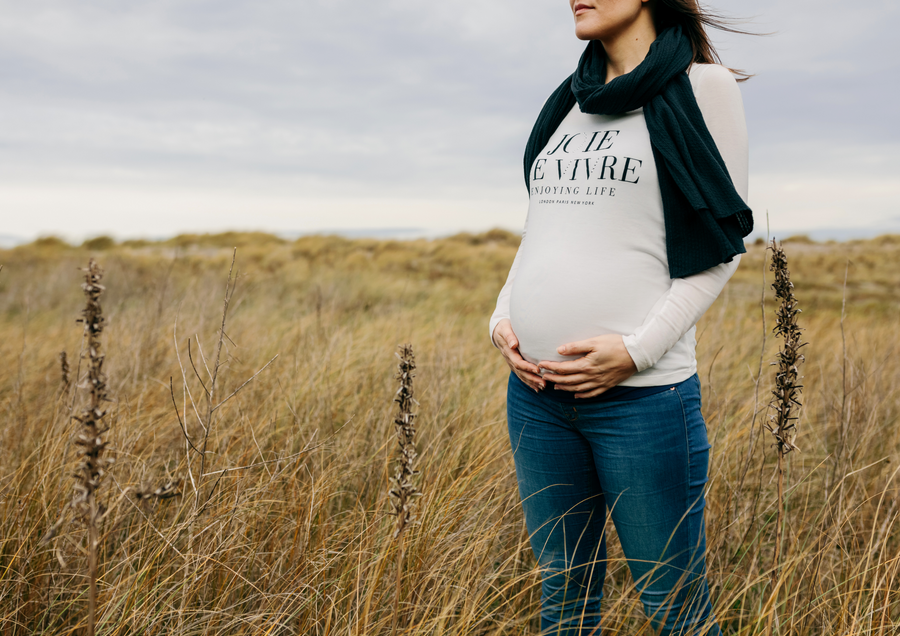 a pregnant woman standing in a field of tall grass 