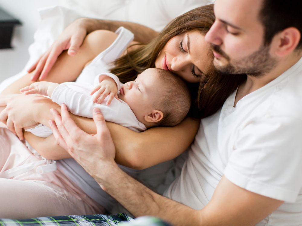 A mother and father lying on a bed, holding their baby close, radiating love and tenderness 