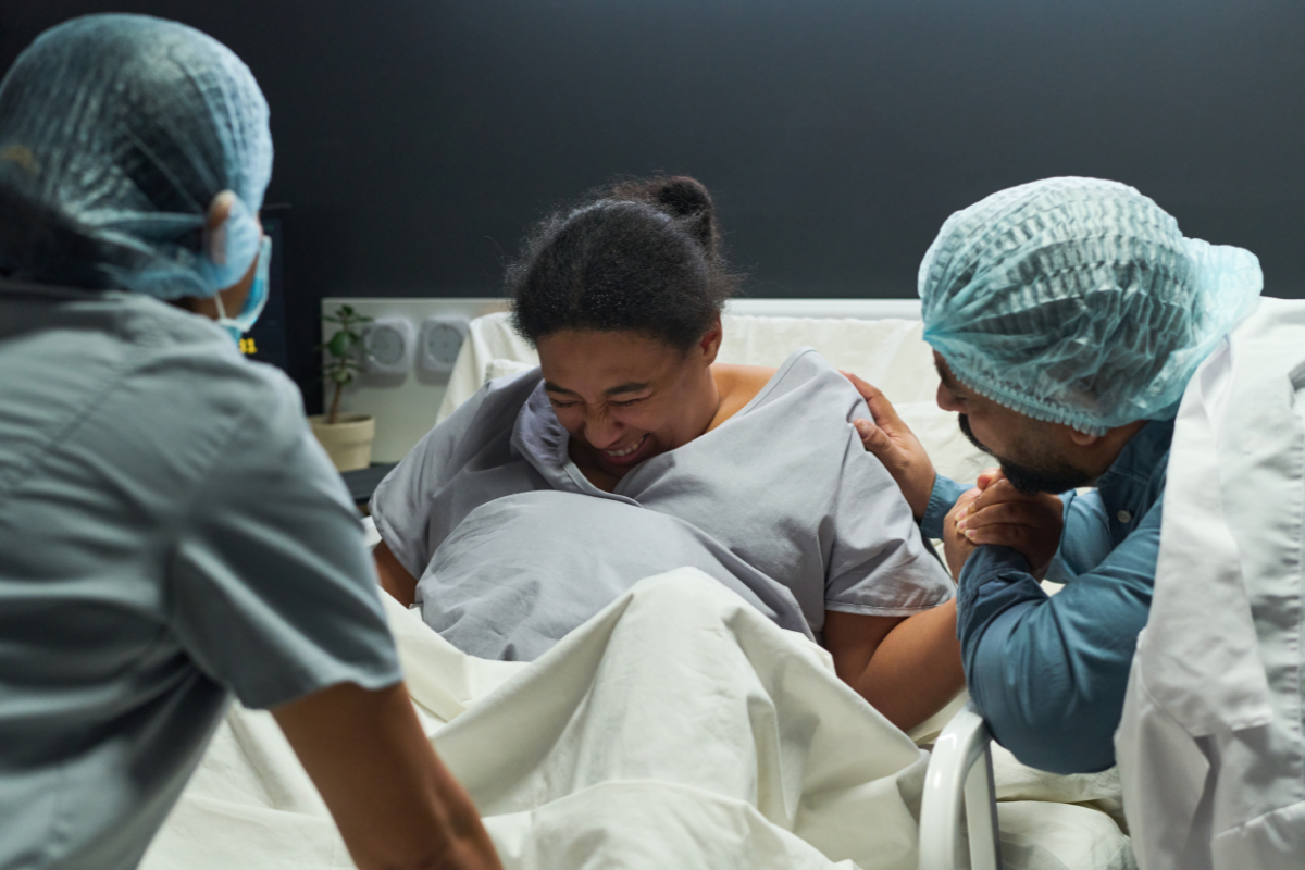 Birth partner beside a woman during the pushing stage of labour, both wearing hospital gowns in a hospital setting.