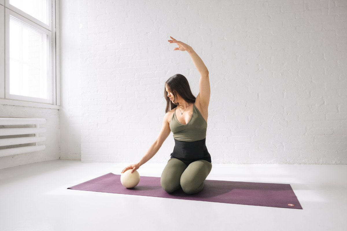 Woman wearing a postpartum support belt while doing Pilates exercises with a ball on a mat