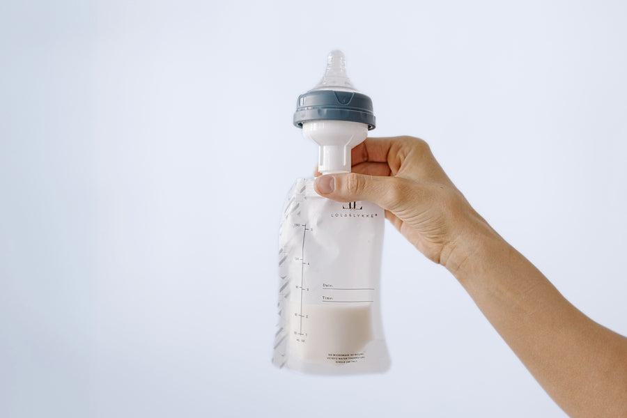  A hand holding a Lola&Lykke Breast Milk Storage Bag with an adapter, designed for easy storage and feeding with a single product.