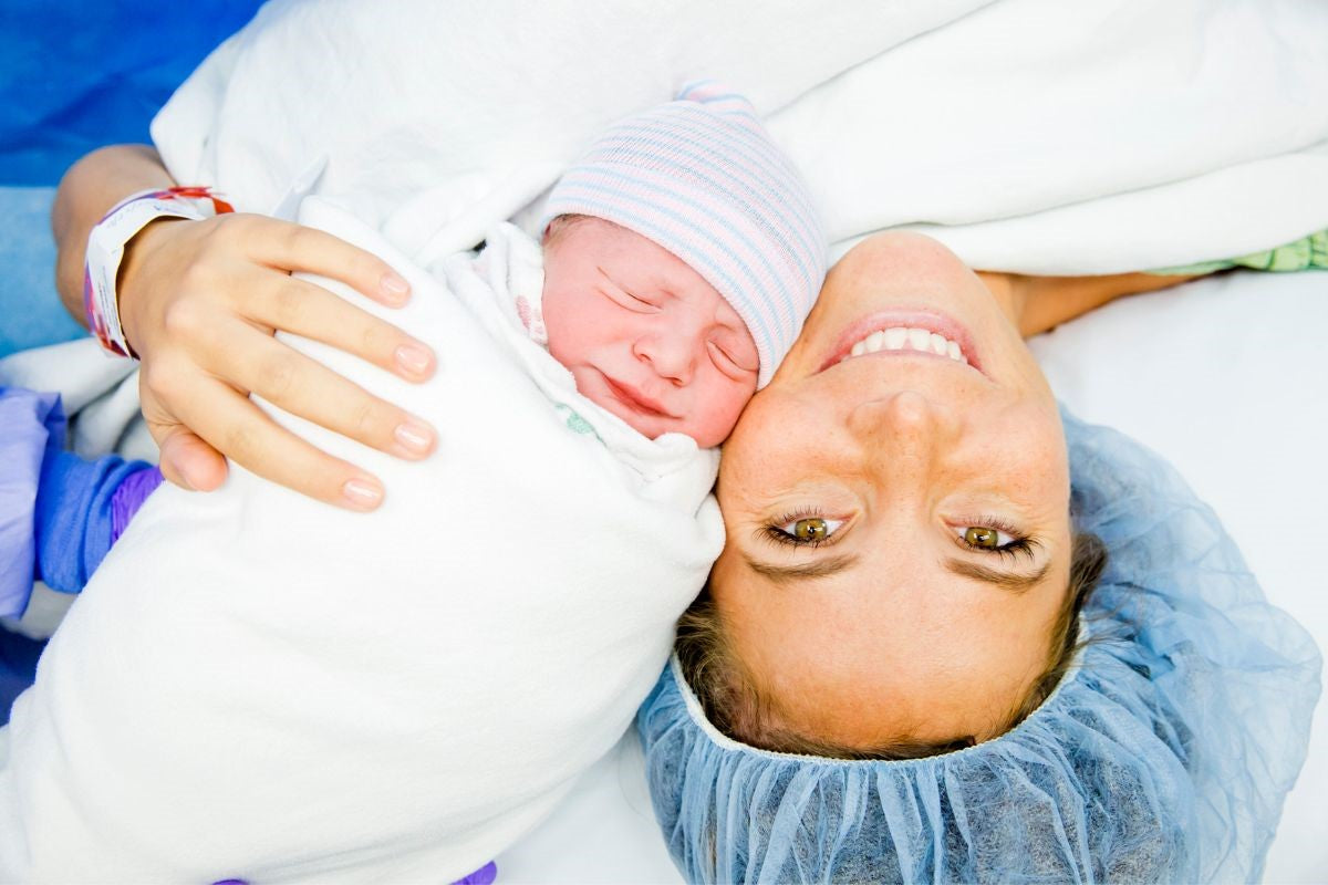 A mum is looking up the camera and smiling, while holding her new born baby