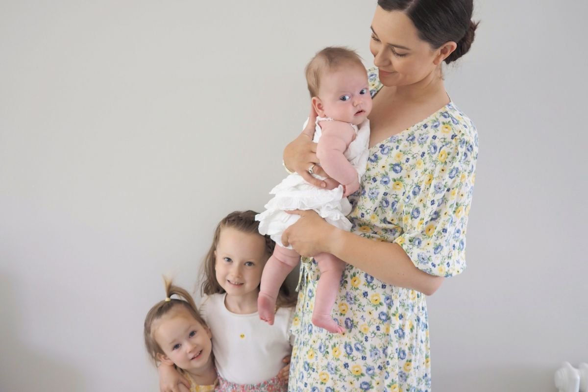 Midwife Madison holding her baby while her two happy daughters stand next to her, a loving and nurturing family scene