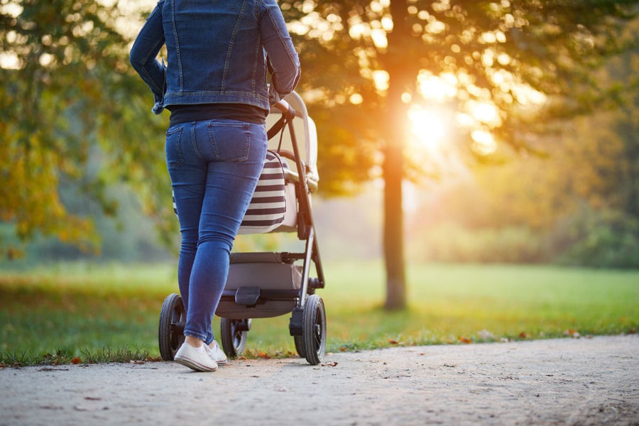 A mum is on a walk in park with her baby in a stroller, with beautiful sunset at the background