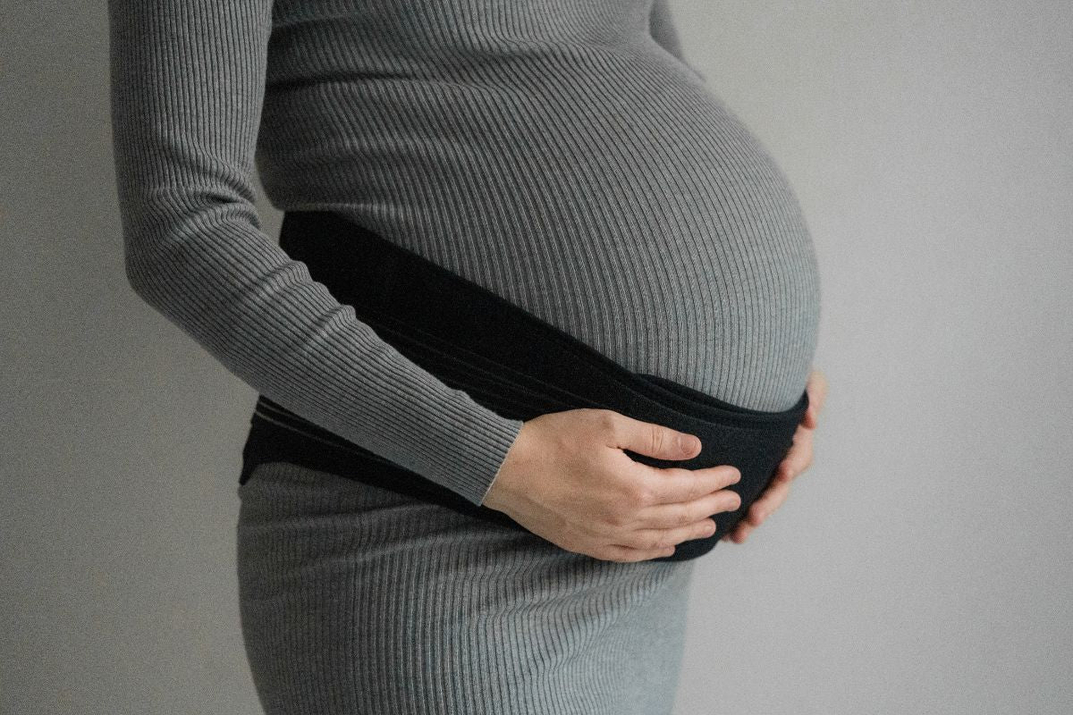 A woman wearing a pregnancy support belt while holding her stomach with both hands