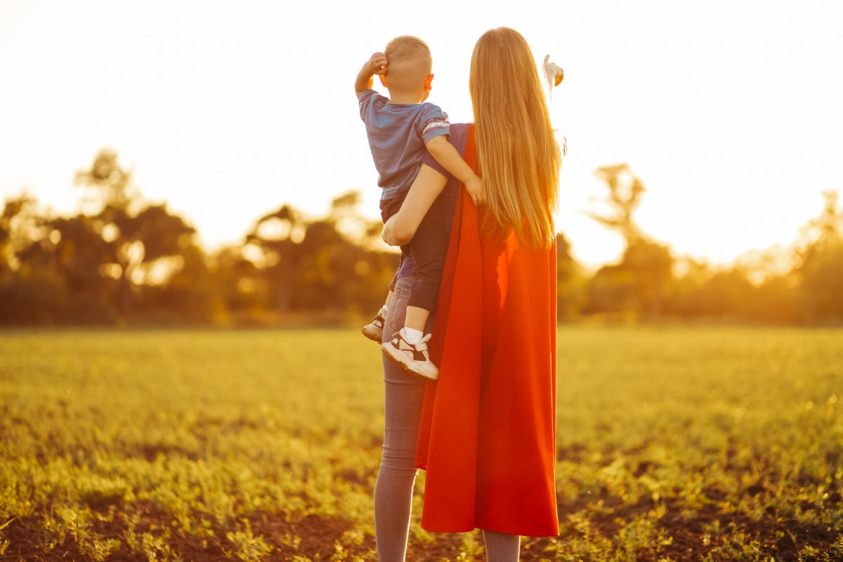 An amazing mum holding her child while wearing a superhero cape