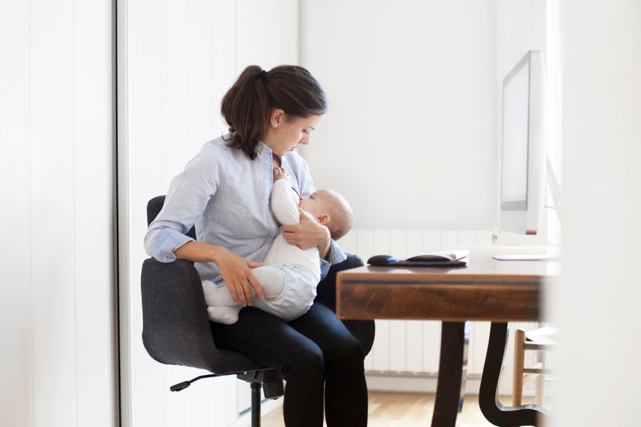 A mother breastfeeding her baby at work, wearing a button-down shirt designed for easy breastfeeding access.