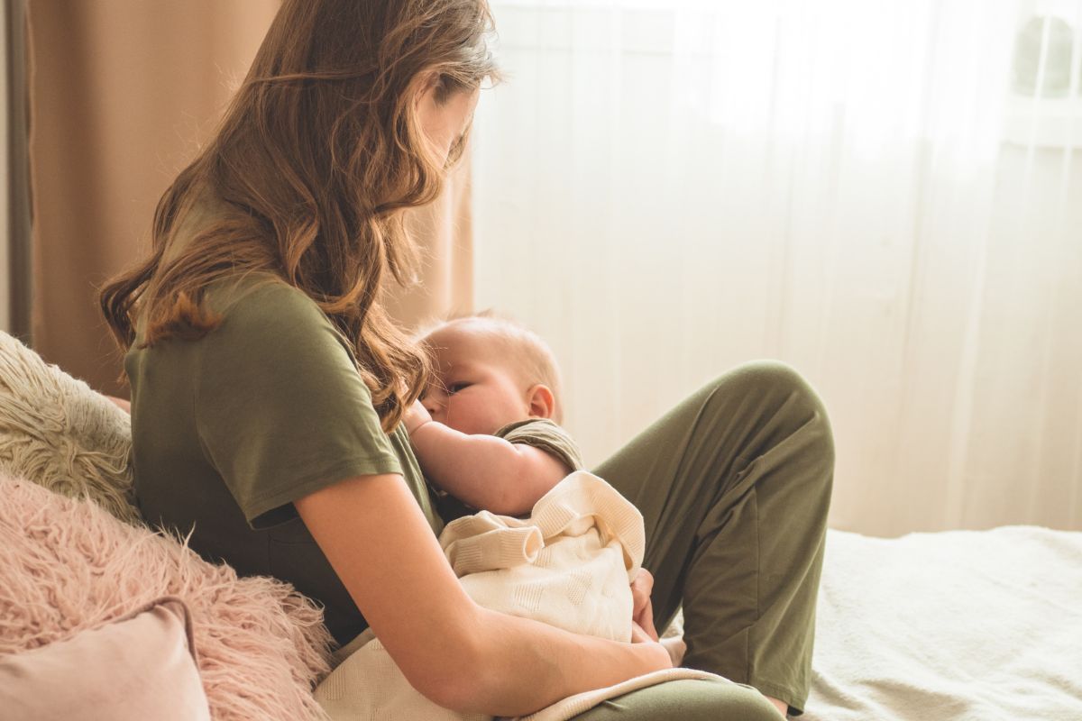A mother with brown hair breastfeeding her baby on a bed