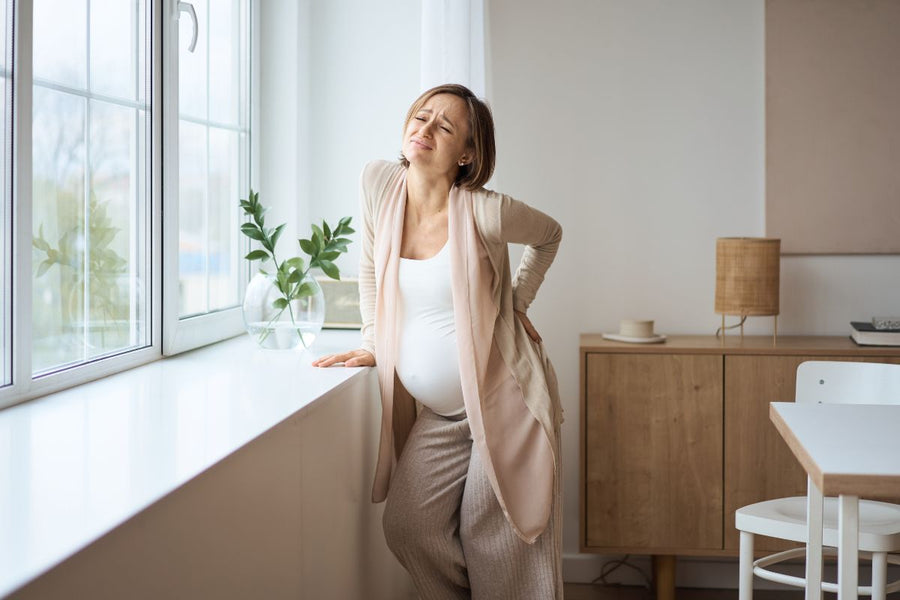 A pregnant women suffering from tailbone pain is leaning against a counter
