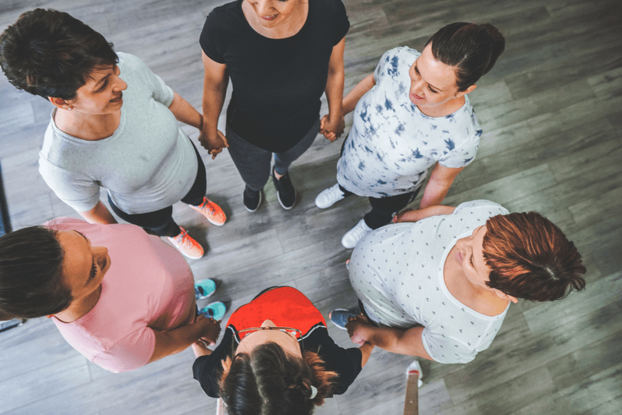 Six women standing in a circle and holding each others’ hands