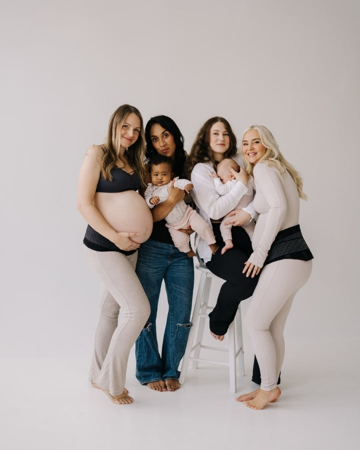 Four women, two pregnant and two with babies, posing together on a white background and using maternity belts.
