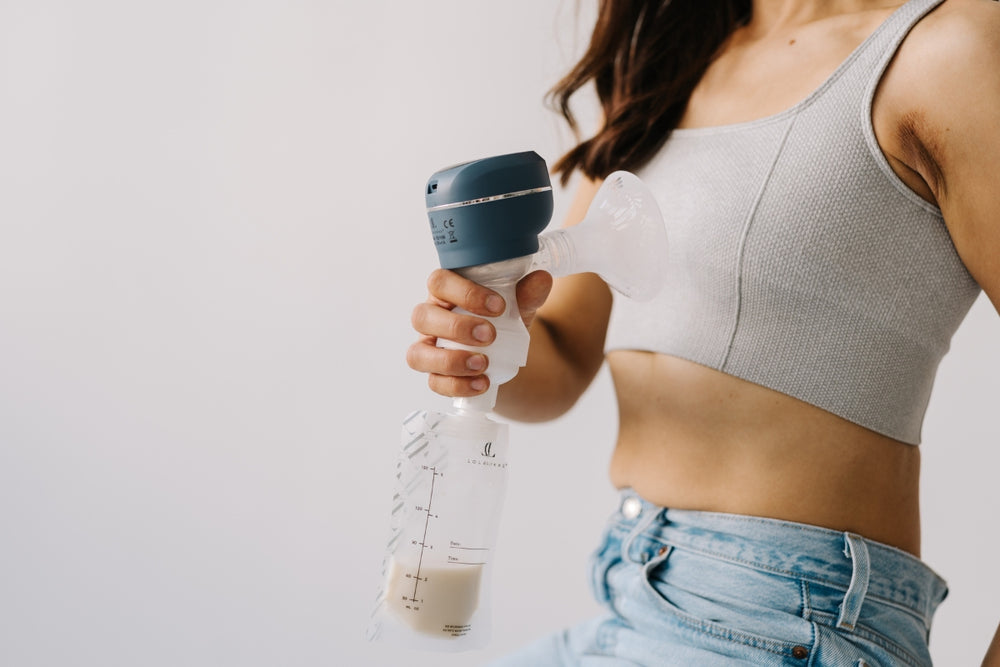 Close-up of a breast pump expressing milk directly into a storage bag, illustrating the Lola&Lykke complete feeding solution.