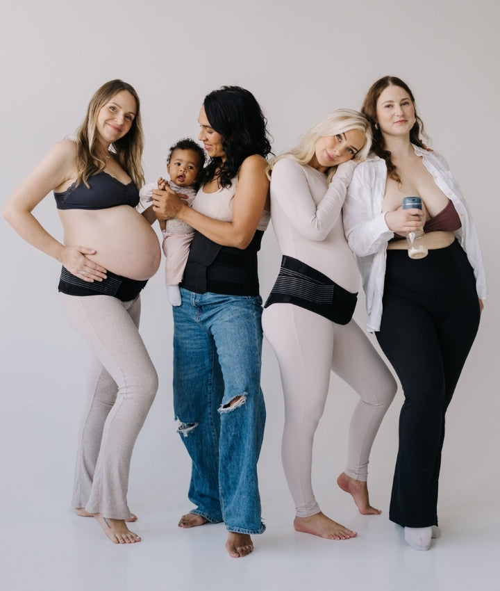 Four women standing together against a white background, one holding her baby, one using a breast pump, all wearing maternity belts, showcasing postpartum and breastfeeding support.