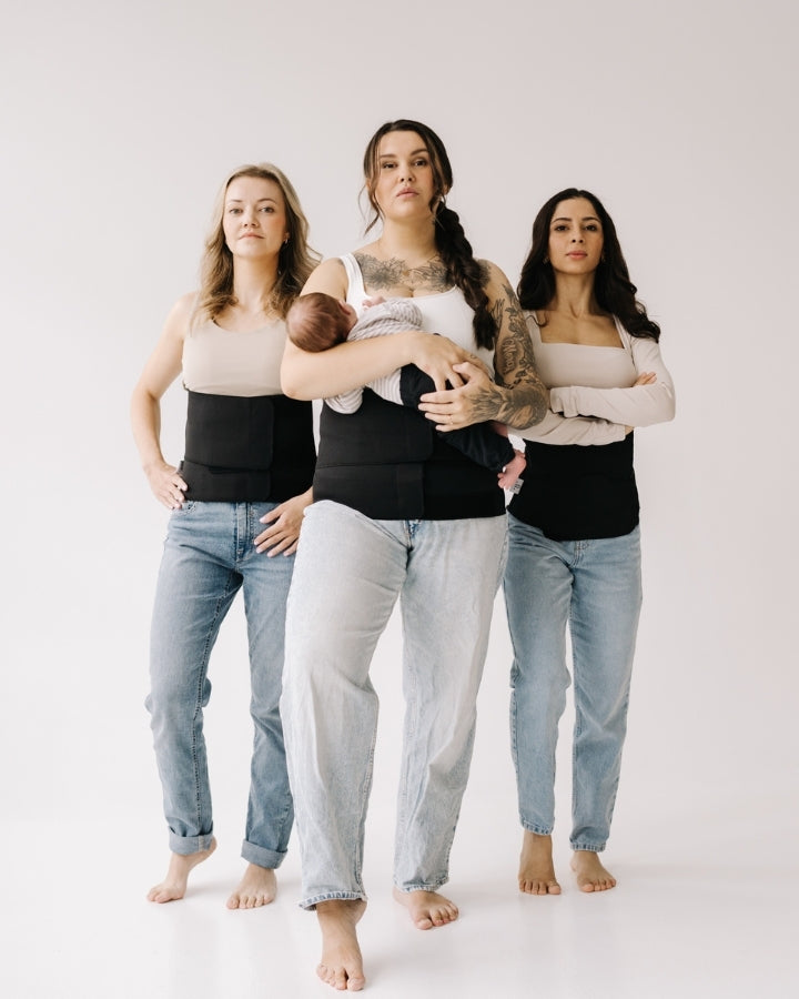Three women standing side by side against a plain background, all wearing postpartum recovery bands, with one woman holding her baby, illustrating postpartum support.