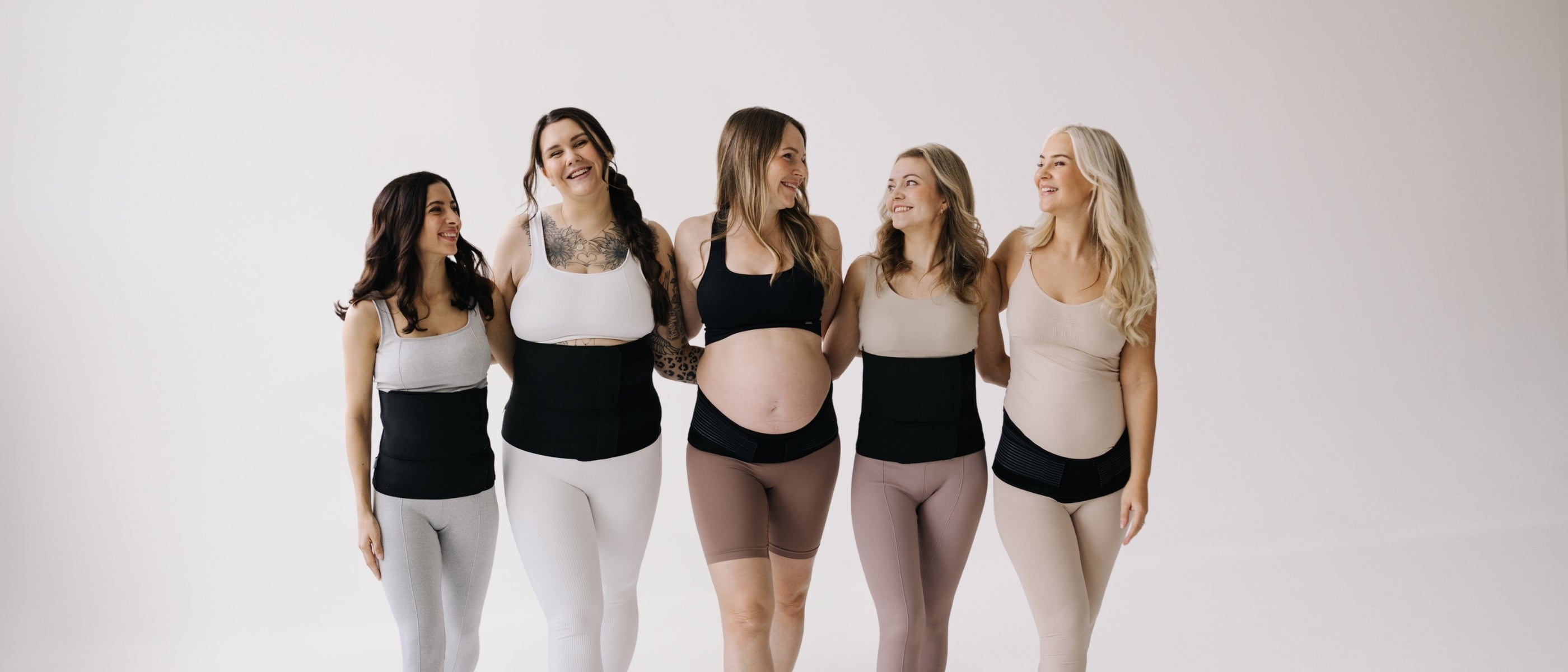 Five women wearing maternity support bands on a plain background