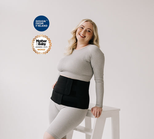 Woman wearing a black maternity support belt, sitting on a white stool with 'Design from Finland' and 'Mother&Baby Awards 2023 Bronze' logos in the corner.